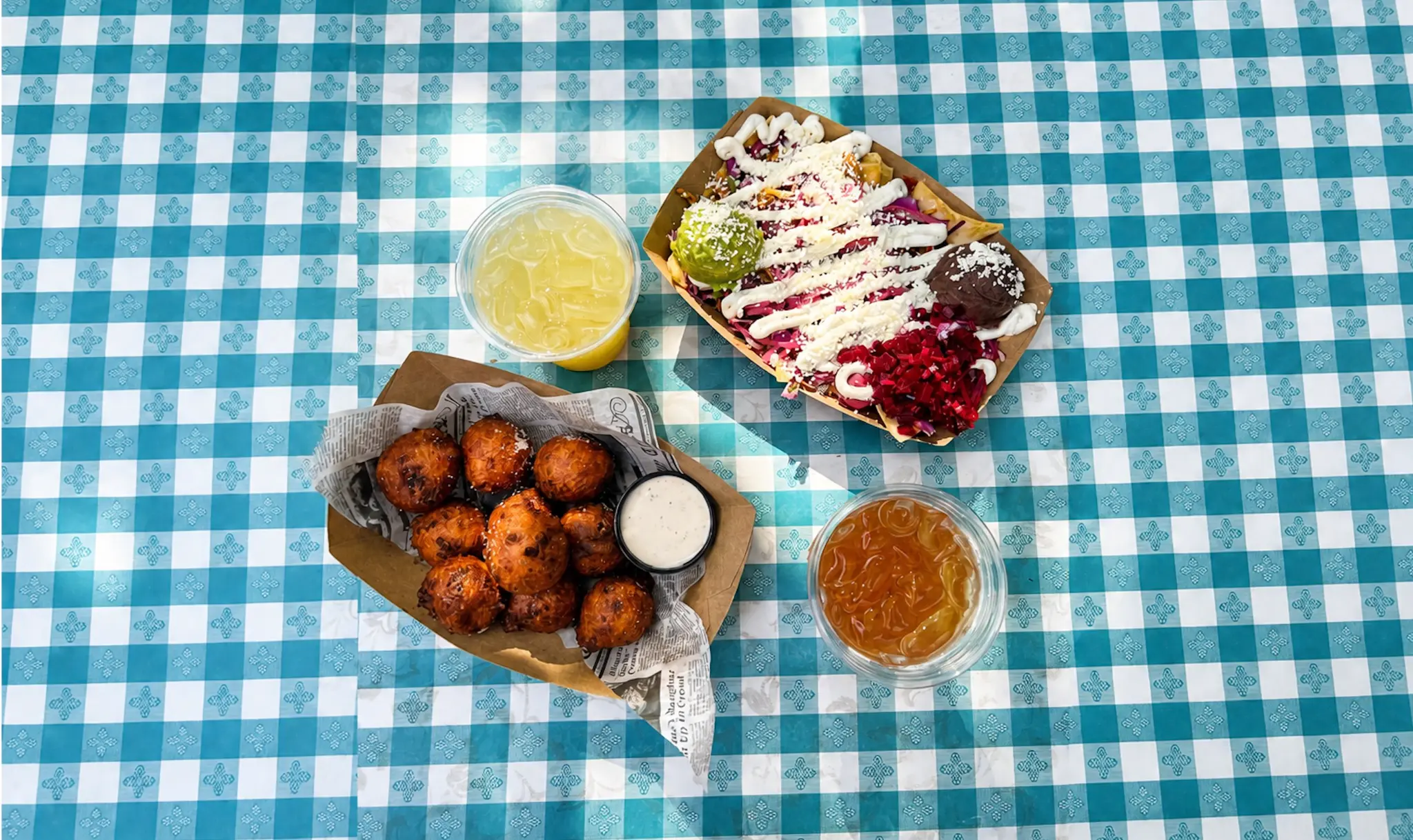 Jalapeño hushpuppies, tacos, and drinks on a blue gingham table at Austin Daily Press in East Austin
